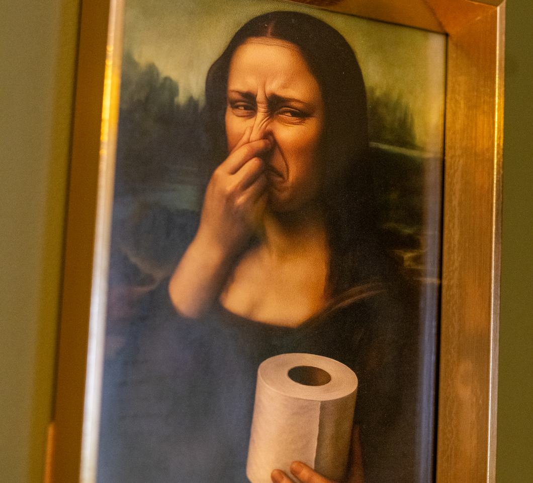 Żartobliwy obraz w złotej ramie — Mona Lisa zatyka nos i trzyma rolkę papieru toaletowego